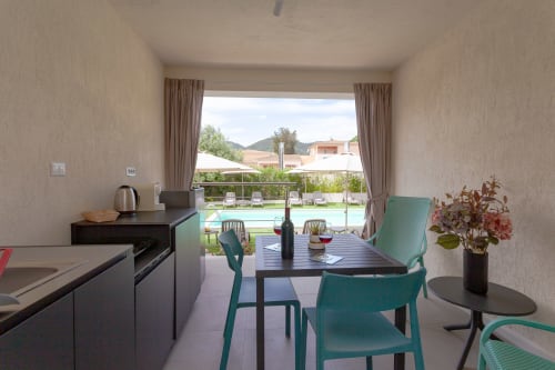 King room with pool view balcony at Le Dune Relax, San Teodoro. Modern dining area overlooking swimming pool and grounds.