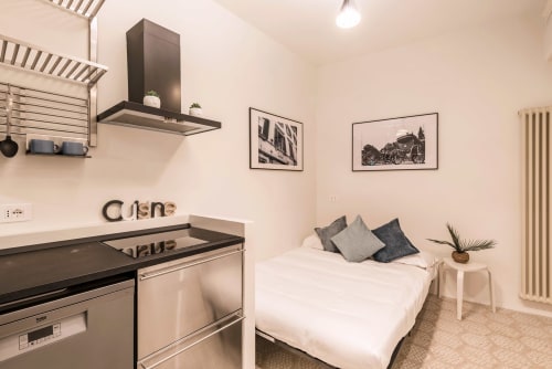 Monolocale moderno a Roma con angolo cottura, letto con cuscini, cappa nera e arredamento minimalista