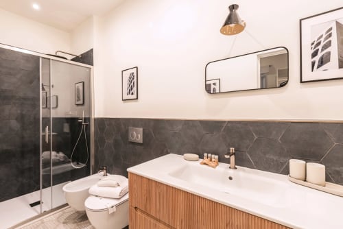 Bagno moderno presso Flavia's Holiday Home a Roma con piastrelle esagonali scure, vanity bianco, doccia in vetro e accessori in ottone