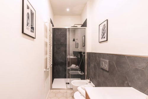 Bagno moderno nella casa vacanze Flavia a Roma con doccia in marmo scuro, lavandino bianco e quadri decorativi