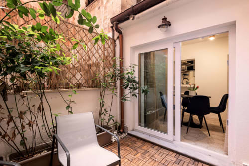 Patio moderno della Casa Vacanze di Flavia a Roma con lettino, piante in vaso, pergolato e porte in vetro che si aprono sull'interno