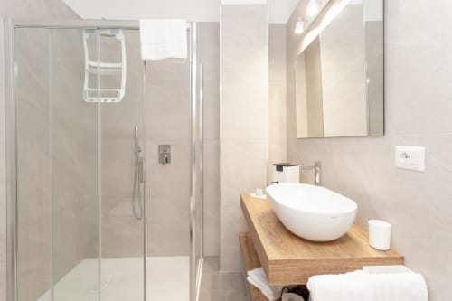 Modern bathroom at Le Dune Relax hotel with white vessel sink, wooden vanity, walk-in shower, and beige tile walls in San
