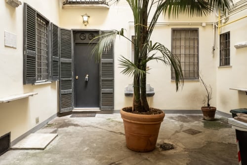 Ingresso della corte di Flavia's Holiday Home a Roma con piante di palma in vaso e porta in legno scuro con persiane