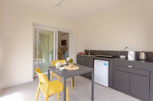 Modern kitchenette with gray cabinetry, yellow chairs, and garden view at Le Dune Relax hotel