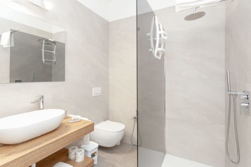 Modern bathroom at Le Dune Relax hotel with white vessel sink, wall-mounted toilet, rainfall showerhead, and wooden vanity in