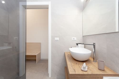 Modern bathroom at Le Dune Relax hotel with white round vessel sink, wooden vanity, and gray tile walls in San Teodoro