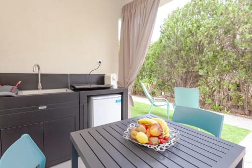 Outdoor patio at Le Dune Relax hotel in San Teodoro with dining table, fresh fruit bowl, kitchenette, and garden views