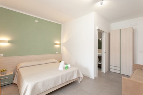 Spacious quadrupla room at Le Dune Relax hotel in San Teodoro with green accent wall, bed, wardrobe, and pool view
