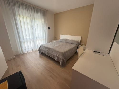 Modern bedroom at Hotel Panorama Lido di Jesolo with queen bed, white headboard, sheer curtains, and wooden floors