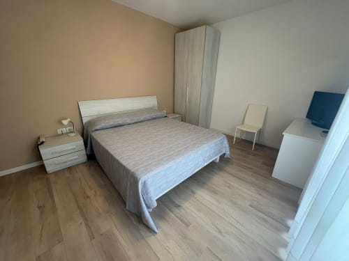 Modern bedroom at Hotel Panorama Lido di Jesolo with queen bed, nightstand, wardrobe, and TV in a bright, minimalist interior