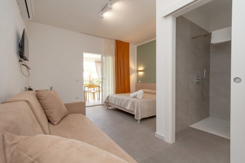 Modern quadruple room at Le Dune Relax hotel in San Teodoro with bed, sofa, ensuite bathroom and balcony access