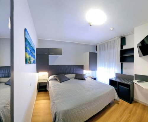 Modern double bedroom at Hotel Panorama Lido di Jesolo with flat-screen TV, dark headboard, white bedding, and contemporary