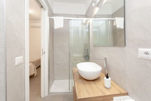 Modern bathroom at Le Dune Relax hotel in San Teodoro with white round sink, wooden vanity, and glass shower enclosure