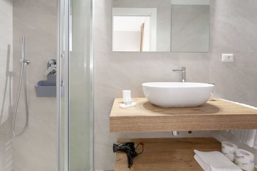 Modern bathroom in Tripla deluxe room at Le Dune Relax, San Teodoro with white vessel sink, wooden vanity, and walk-in shower