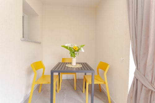 Bright garden view dining nook at Le Dune Relax with yellow chairs, gray table, and fresh flowers