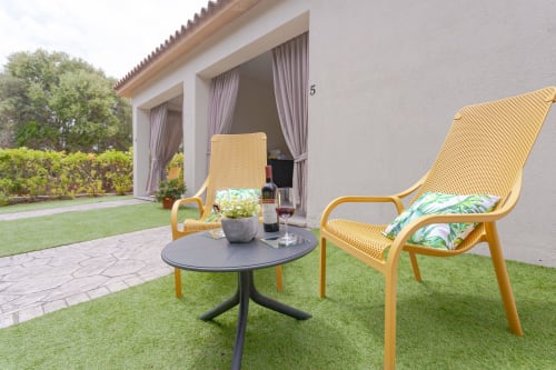 Garden patio seating at Le Dune Relax hotel with yellow chairs, round table, and view of Tripla deluxe room in San Teodoro