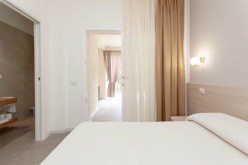Modern bedroom at Le Dune Relax hotel in San Teodoro with white bedding, garden view curtains, and ensuite bathroom