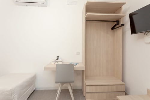 Modern hotel room at Le Dune Relax with wooden wardrobe, desk, bed, TV, and AC unit in San Teodoro
