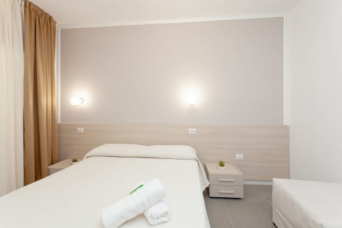 Spacious triple deluxe bedroom at Le Dune Relax hotel in San Teodoro with two beds, light wood headboard, and garden view