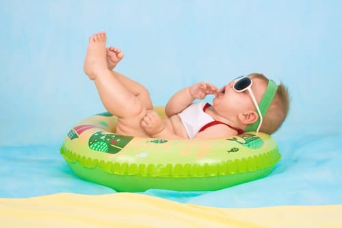 Bébé en lunettes de soleil flottant sur un anneau de piscine vert à la plage près du resort hôtel Cholet