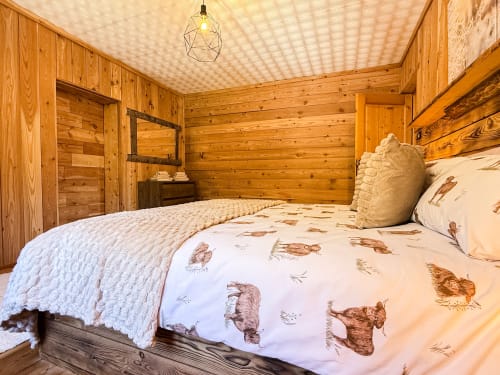 Accogliente camera da letto in legno presso Mountains Properties ad Auronzo di Cadore con biancheria animalier e lampada a sospensione geometrica