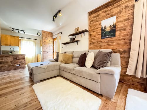 Accogliente appartamento ad Auronzo di Cadore con divano componibile beige, parete in legno e quadri con vista montagna.