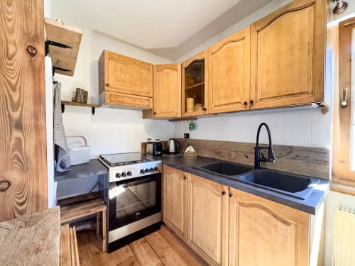 Moderna cucina con mobili in legno, top nero, fornello e lavello in acciaio inox nell'appartamento in montagna ad Auronzo di Cadore