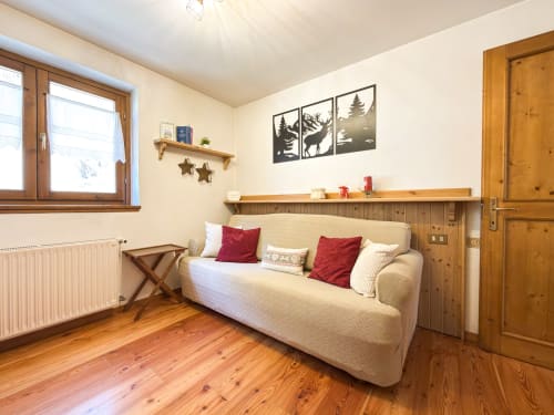 Accogliente camera di montagna ad Auronzo di Cadore con divano color crema, arredi in legno, cuscini rossi e arte alpina