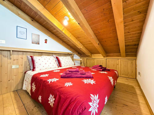 Accogliente camera da letto alpina con biancheria floreale rossa, travi in legno e vista sulle montagne ad Auronzo di Cadore