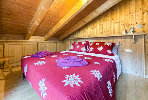 Accogliente camera da letto in chalet di legno ad Auronzo di Cadore con biancheria rossa floreale, travi a vista e asciugamani viola