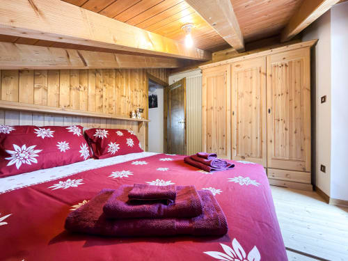 Camera da letto in chalet in legno con biancheria floreale rossa, asciugamani piegati, travi a vista e guardaroba in legno di pino ad Auronzo di Cadore