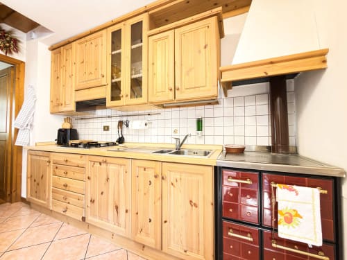 Cucina in legno con mobili in pino, rivestimento piastrelle bianche, fornello a gas e forno rosso nella proprietà di montagna di Auronzo di Cadore