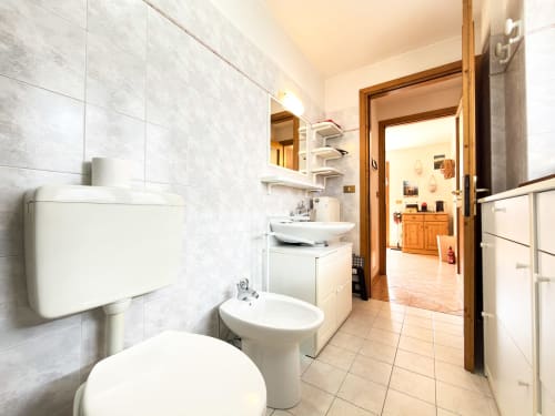 Bagno moderno dell'hotel Auronzo di Cadore con piastrelle bianche, WC, lavabo su colonna e vanity con specchio
