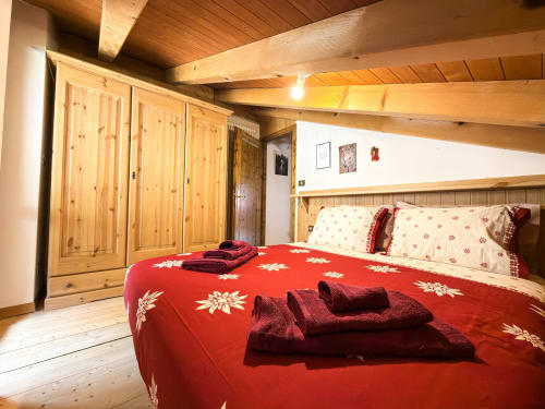 Accogliente camera da letto in legno con biancheria rossa a motivi solari, soffitti con travi, armadio e vista montagna ad Auronzo di Cadore