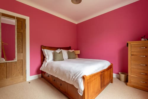 Bright pink bedroom with wooden bed, white bedding, and wooden dresser at Sleeping Betty cottage in Comrie