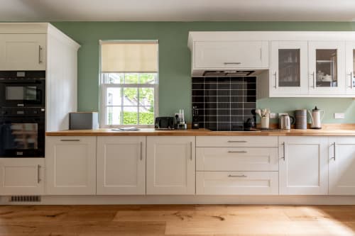 Modern kitchen in Sleeping Betty cottage, Comrie, with cream cabinets, black tile backsplash, wooden counters, and green