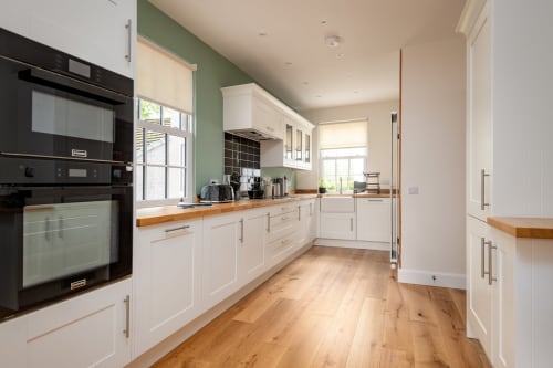 Modern kitchen at Sleeping Betty cottage in Comrie with white cabinetry, wooden countertops, black appliances, and garden