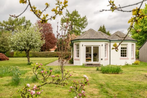 Sleeping Betty cottage Crossloan in Comrie with white exterior, garden view, and blooming pink flowers in manicured grounds