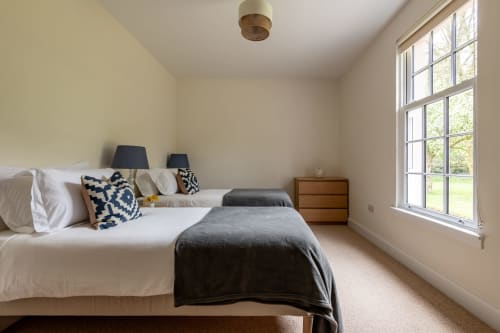 Bright bedroom at Sleeping Betty cottage in Comrie with twin beds, blue patterned cushions, wooden dresser, and garden views
