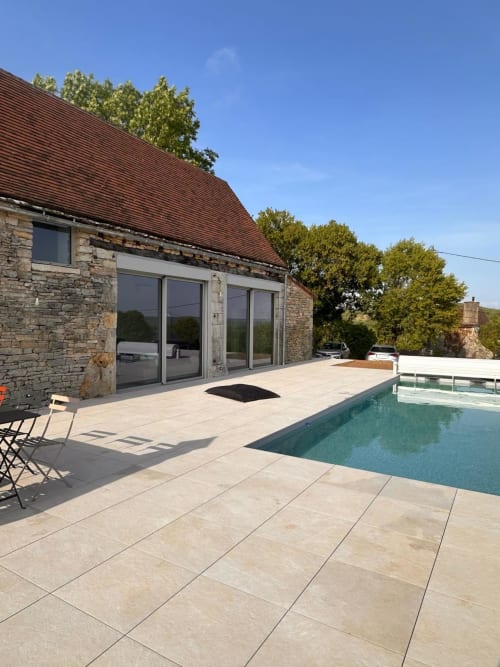 Terrasse piscine contemporaine du Gîte l'Harmonie du Causse avec bâtisse en pierre, portes coulissantes et piscine chauffée en milieu rural