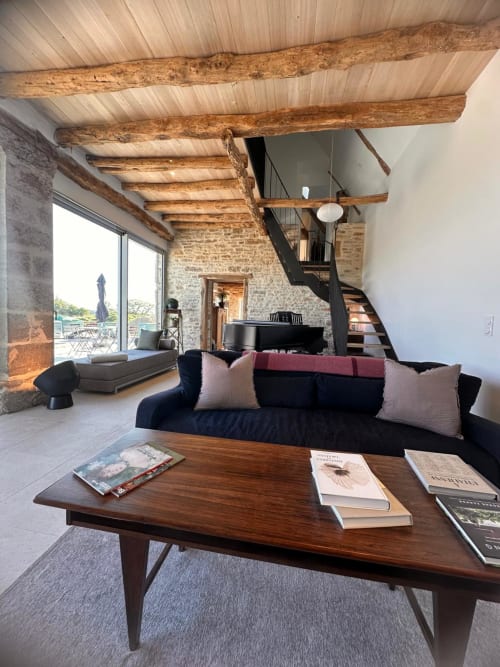 Séjour rustique moderne aux poutres apparentes, canapé noir et murs en pierre au Gîte l'Harmonie du Causse, France