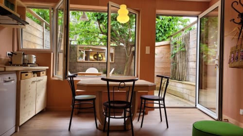 Zona pranzo in tonalità terracotta calda con sedie nere, angolo cottura e vista sul giardino presso Le Lodge du Cap Ferret