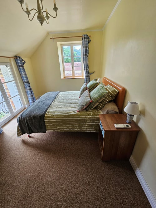 Bright yellow attic bedroom at La Jonchere gatehouse villa with garden view windows, wooden bed, plaid curtains, and brown