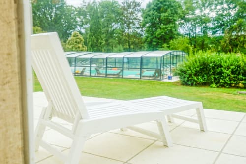 White lounge chair on patio overlooking garden with pool enclosure at La Jonchere villa, Concressault