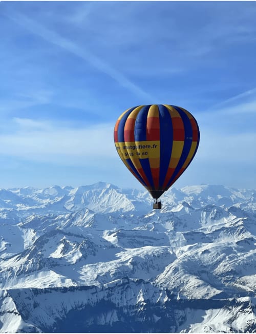 Hot air balloon flying over snow-covered Alps near Notre Dame de Bellecombe, France