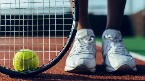 Raquette de tennis avec balle jaune sur court de terre battue, baskets blanches, hôtel Chez Francine