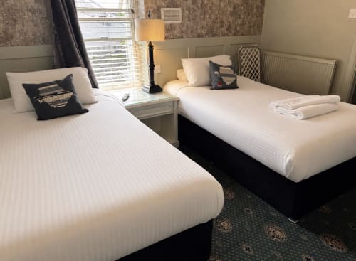Twin bedroom at Gwesty Holland Hotel with two beds, lamp, radiator, and windows overlooking Llanfachraeth