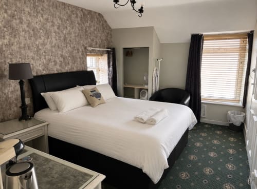 Standard Double Room at Gwesty Holland Hotel in Holyhead with black bed, white linens, patterned wallpaper, and windows with