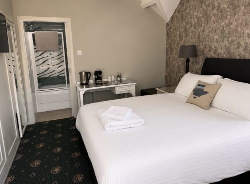Modern double bedroom at Gwesty Holland Hotel with white bedding, dark headboard, desk, and ensuite bathroom access