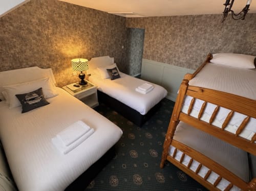 Standard Quadruple Room at Gwesty Holland Hotel featuring four beds with white linens, patterned wallpaper, and warm lighting